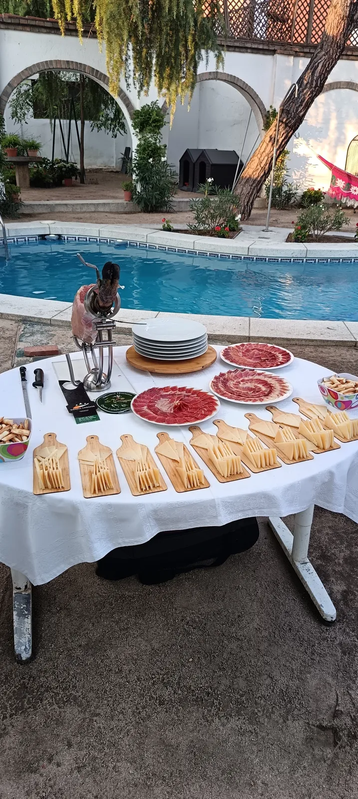 Mesa de jamón y quesos junto a una piscina en un evento privado